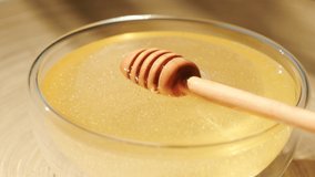 Honey dripping, pouring from honey dipper in a glass bowl. Close-up. Organic Thick honey dipping from the wooden honey spoon, closeup. 4K UHD video footage. Slow motion