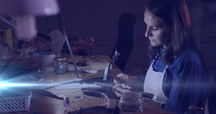 Animation of glowing light over caucasian woman using tools working in workshop. labor day, work, workers, tradition and celebration concept digitally generated video.