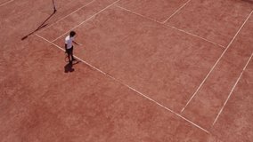 Afro American guy professional tennis player playing tennis in a sunny day on the large tennis court outdoor taking video with drone birds eye view