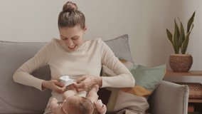 Medium slowmo of happy young mother putting tiny white socks on little feet of her newborn baby sitting on sofa at home - Powered by Shutterstock - Get 15% off with code: PIKWIZARD15