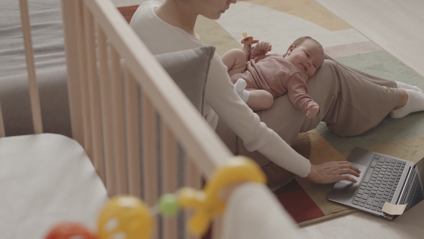 Slowmo of young Caucasian woman with infant daughter lying on her laps working on laptop from cozy home - Powered by Shutterstock - Get 15% off with code: PIKWIZARD15