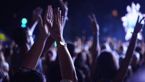 People silhouettes clapping, waving hands on live music concert at open air festival. Fans applause at favourite band performance in slow motion. Bright colorful stage lighting. - Powered by Shutterstock - Get 15% off with code: PIKWIZARD15