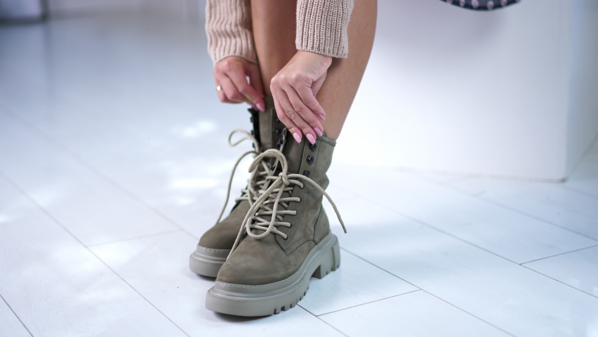 Model ties the laces on the modern boots. Sitting female demonstrating grey fashionable footwear. Close up. | Shutterstock HD Video #1094051441