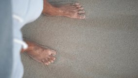 Feet on the beach shore top view. A wave washes them. Vertical video.