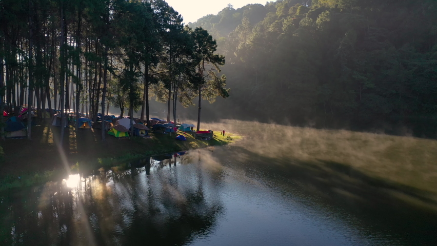 Aerial drone view of dreamy gold mist on water surface in winter with light beams shining through the trees at famous Pang Ung national park, Mae hong son, Thailand | Shutterstock HD Video #1094057127