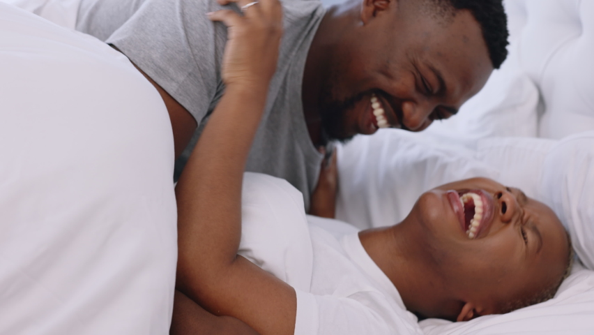 Happy playful black couple smile in bed at home and laugh together. Romantic man and woman bonding in their bedroom in the morning. Carefree boyfriend and girlfriend romance, funny and intimate Royalty-Free Stock Footage #1094061883