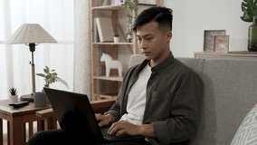 asian male creative worker is waving and explaining to his client with hand gestures while having an online meeting on the computer in the living room at home.