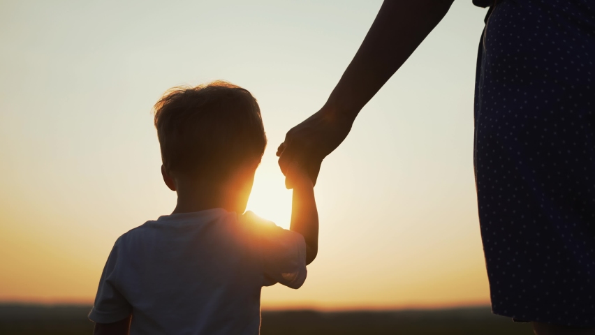Happy family concept. Mom with baby is walk on grass in park.Mother with boy in field at sunset. Girl holds child by hand.Active lifestyle concept.Happy boy holds his mother by hand and walk on grass. | Shutterstock HD Video #1094063661