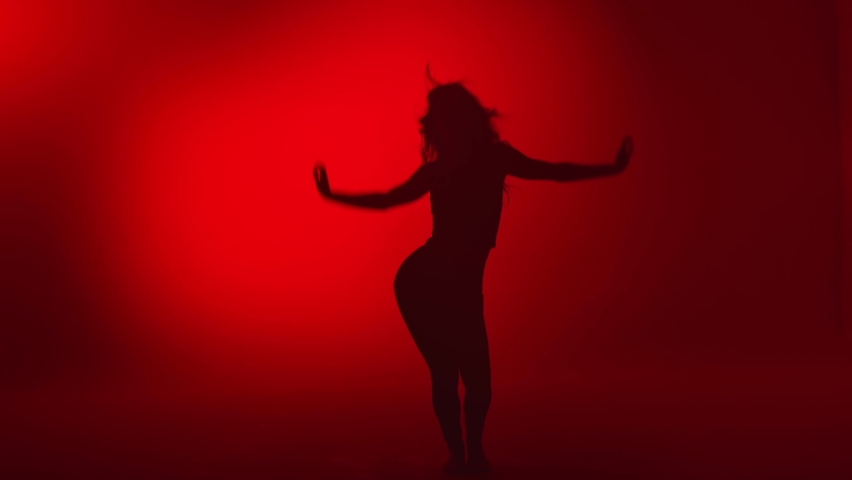  silhouette performing professional choreography isolated on red studio background slow motion. Seductive flexible lady dancing waving hair feeling pleasure. 
