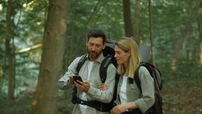 Active date. Positive middle aged spouses with backpack walking in forest, man showing route to his woman on mobile navigation app, tracking shot, slow motion - Powered by Shutterstock - Get 15% off with code: PIKWIZARD15