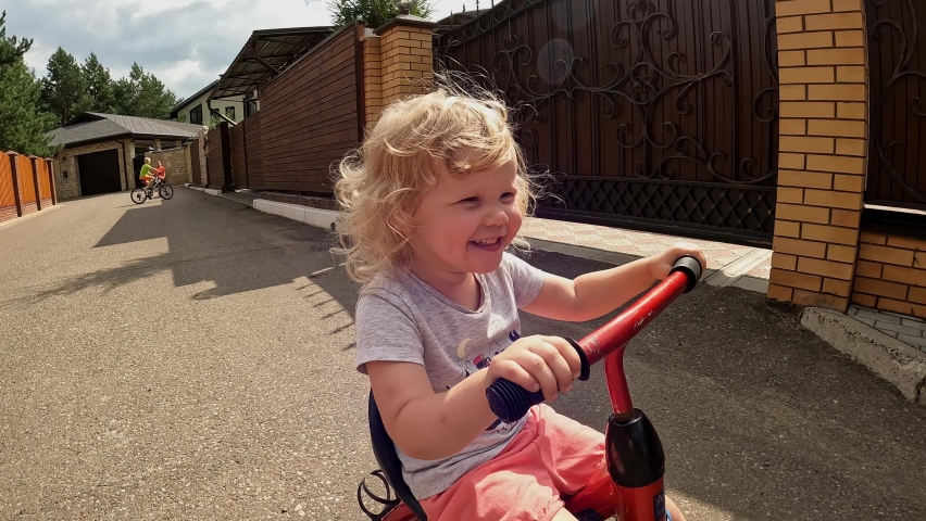 Happy curly blonde girl riding on cycle laughing enjoy happy childhood steadicam establish shot closeup overjoyed little baby smiling driving bike bicycle relaxing outdoor sports leisure activity Royalty-Free Stock Footage #1094072717