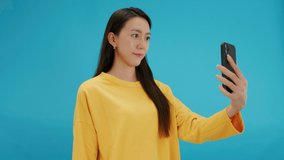 Young Beautiful Asian woman hand holding mobile phone taking photo. Happy attractive girl enjoy taking smile selfie with smartphone express exited and positive emotion. isolated on blue background