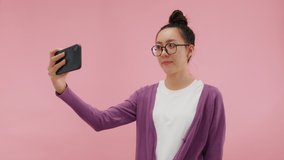 Young Beautiful Asian woman hand holding mobile phone taking photo. Happy attractive girl enjoy taking smile selfie with smartphone express exited and positive emotion. isolated on pink background