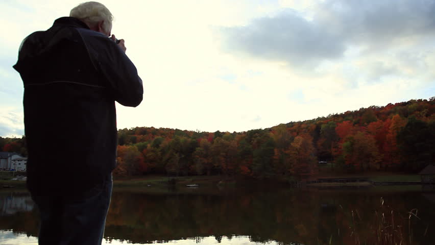 A man taking pictures of the autumn leaves.  Camera reveals the sun as it moves.