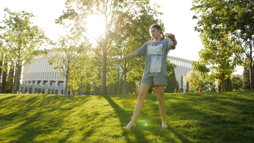 A teenage girl does gymnastic exercises in the park at sunset.