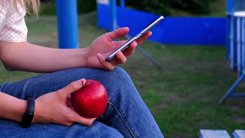 A student, a schoolboy with an apple in his hands and a smartphone outdoors. Close-up of female hands using a smartphone to search for content, or communicate.