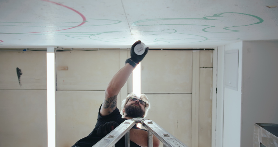 A graffiti artist draws on the wall of a contemporary art gallery. View from below