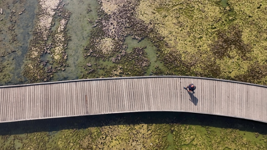 Man walking on a long wooden old bridge over a dried beach in the mediterranean