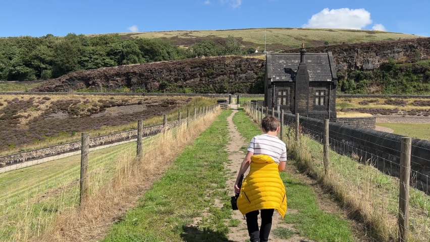 Boy walking along a path at on the dam wall at Butterley Reservoir Martsden Huddersfield West Yorkshire on a summers day.