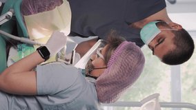 Vertical video, Two dentist doctors in medical masks, a man and a woman in a dental office, perform an operation on the teeth. Dentistry. Healthcare and Medicine Concept.