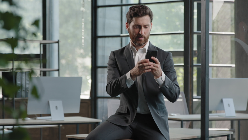 Adult company CEO manager worker boss manager man specialist professional businessman sitting on table in office looking at smartphone screen using mobile phone chatting online check data organizer | Shutterstock HD Video #1094091869