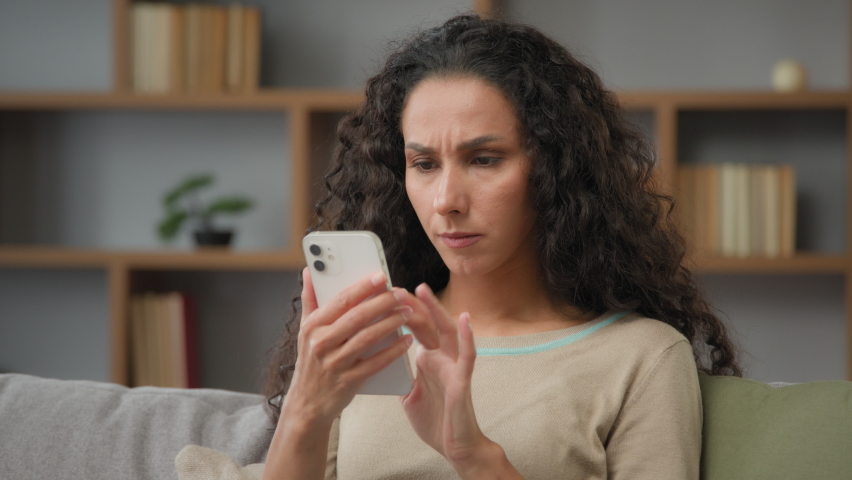 Hispanic sad displeased woman has problem with online mobile app on cell phone unhappy with blocked account in social networks looking at cellphone screen scam unsuccessful bad news sitting at home Royalty-Free Stock Footage #1094091877