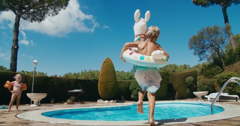 Happy children on summer vacation run and jump in to the swimming pool with inflatable lama ring on travel. Colourful summertime slow motion footage. Family on resort at holidayの動画素材