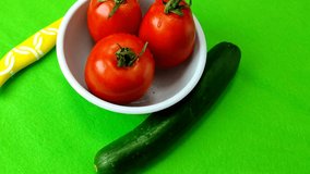 Cucumber and tomato in a small white plate and yellow knife on a beautiful green background, 4k video from above