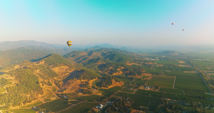 Three hot air balloons in the clear blue skies over amazing scenery. Flying aerostats in green valley of Napa, California, USA.