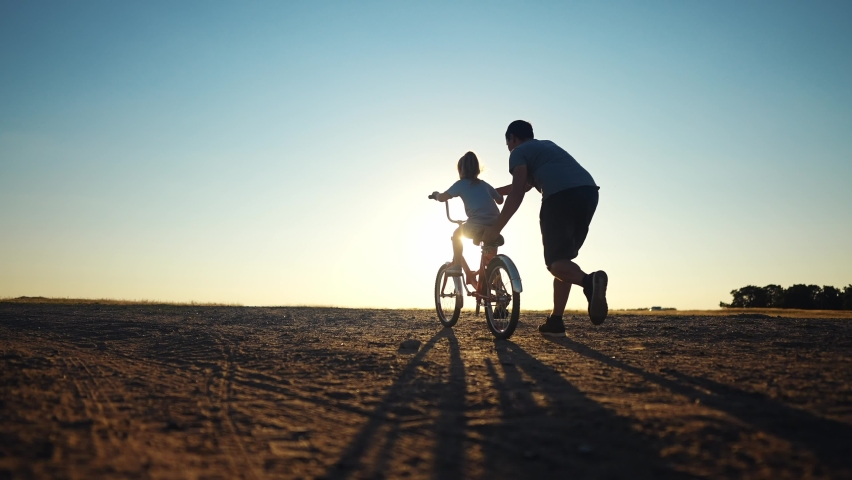 dad teaches daughter to ride a bike. happy family childhood dream concept. father and little daughter learn to ride a bike silhouette in the park. happy family goes in for sports sunlight outdoors Royalty-Free Stock Footage #1094107429