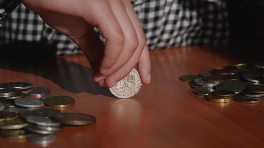 Human hands twist the coin, it rotates on the table. Fortune telling, heads and tails, coincidence, chance. Concept of financial literacy.Unrecognizable girl playing with coins slow motion 200 FPS.