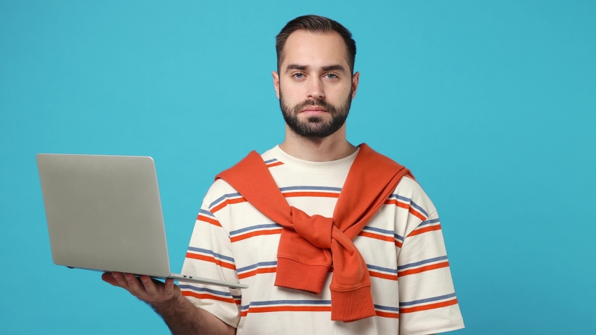 Young brunet man 20s wears striped t-shirt hold use work on laptop pc computer typing say yes just found out great big win news do winner gesture isolated on plain pastel light blue background studio