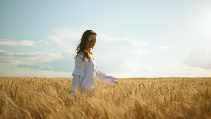 carefree woman is running on ripe rye ears in agricultural fields in sunny summer day, slow motion