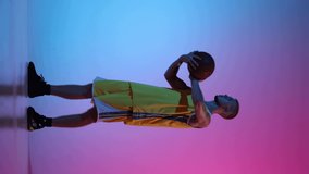 Skills. Young man, basketball player spinning basketball ball on his finger at studio over gradient blue pink neon background. Sport, action, motion, skill concept.