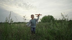 A boy runs on the grass with an airplane in his hands. A child flies in his dreams. Active games in nature. Happy and smiling boy. Slow motion video. High quality 4k footage