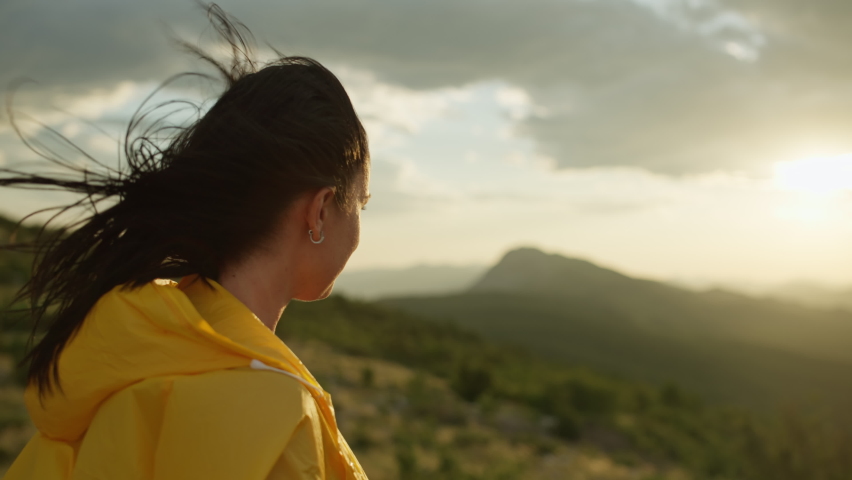 Close-up of a girl on top of a mountain. A person who has conquered the peak looks into the distance at a beautiful mountain landscape during sunset. High quality 4k footage
