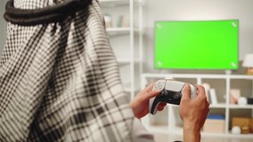 Middle eastern man playing video game, tv with chroma key. Television with green screen, play gaming on modern console. Wearing traditional Islamic male clothes. 