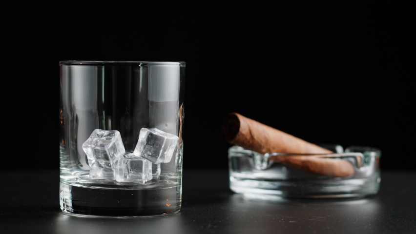 Brandy or whiskey and cigar close-up. Luxury cognac with ice on black background. Alcohol amber drink, drinking rum, liqour beverage in glass. Royalty-Free Stock Footage #1094119057