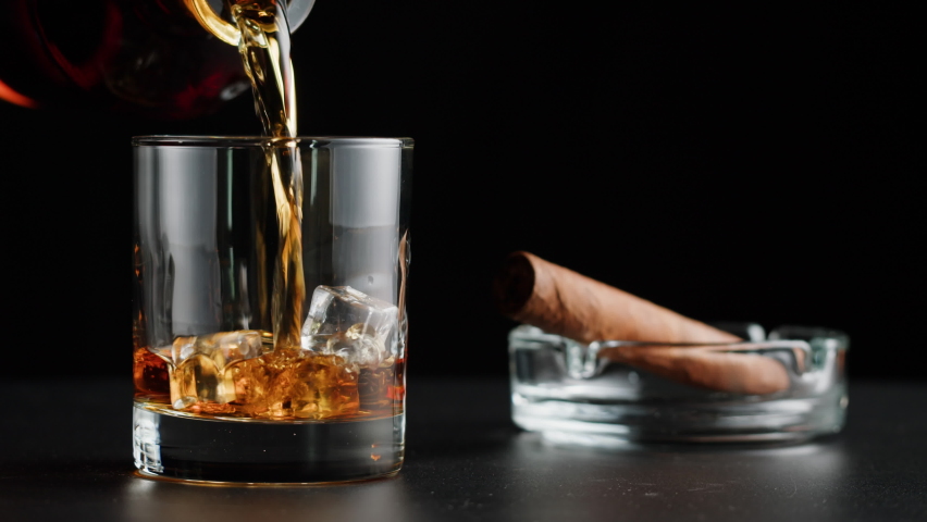 Brandy or whiskey and cigar close-up. Luxury cognac with ice on black background. Alcohol amber drink, drinking rum, liqour beverage in glass. | Shutterstock HD Video #1094119057