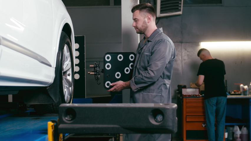 A car service employee installs a wheel adapter with a target on the wheel to perform a wheel alignment. Diagnostics and balancing of wheels of a lifting trolley at a modern service station. | Shutterstock HD Video #1094124211