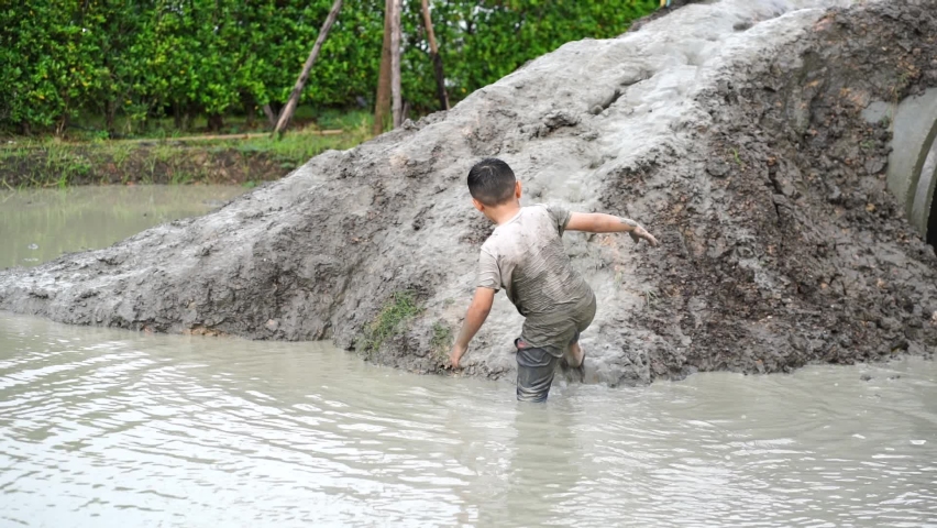 Asian boys enjoy playing in the mud up a hill and then slipping down the mud in a fun way into a pond with a wet, messy t-shirt at a summer camp. Royalty-Free Stock Footage #1094124471