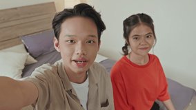 POV of Asian boy and girl looking at camera and speaking while filming vlog at home or chatting on online video call