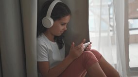 Girl of 10 years communicates with friends via video call. Teens wins a game on the phone at the desk at home in the living room. Happy adult child listens to music, plays games, studies with lessons