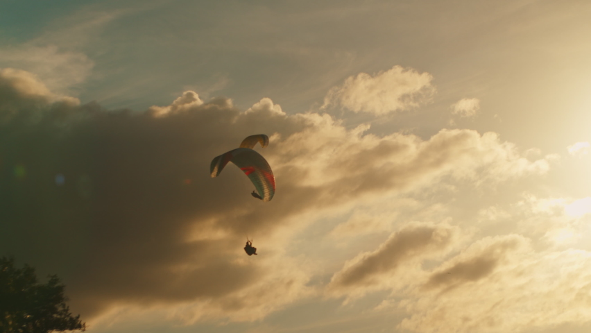 Two paragliders soar in a beautiful golden sky against the sunset. Parachutes or paragliding experience. Extreme sport on a paraglider with a parachute flying against a bright sunny sunset, Royalty-Free Stock Footage #1094141477