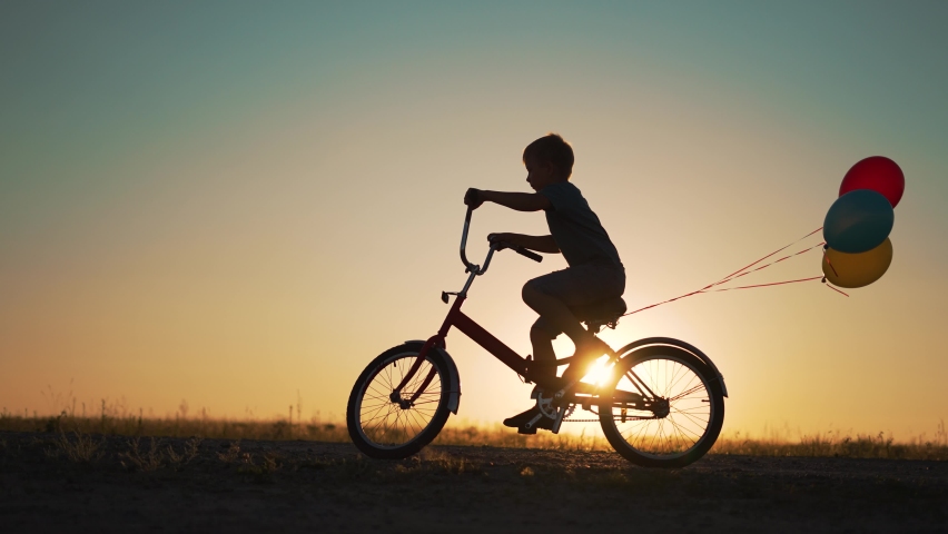 Dream child. Silhouette of child on bicycle plays in park. boy rides through natural green park with balloons. Play with balloons on bike. boy dreams of learning to ride bicycle in nature. Royalty-Free Stock Footage #1094150363