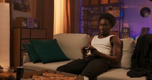 A men of African-American descent spends time in a room on a couch eating a pizza ordered to go, the man holds a pad in his hands, playing a console.