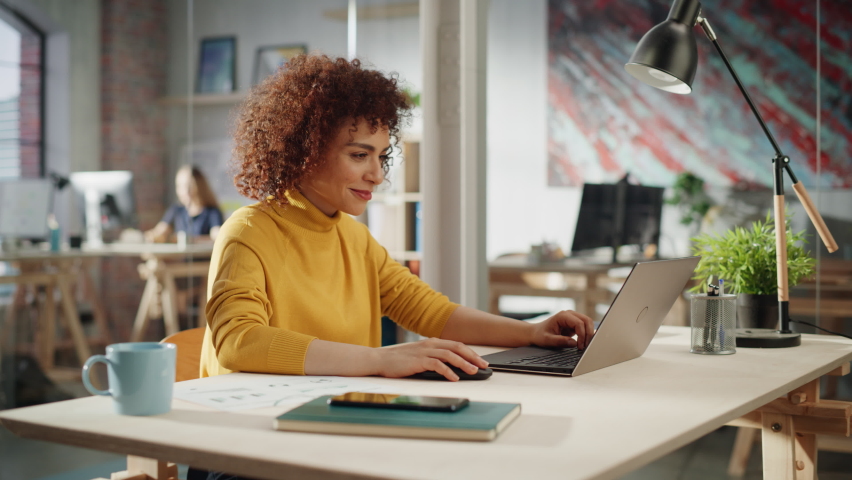 Beautiful Middle Eastern Manager Sitting at a Desk in Creative Office. Young Stylish Female with Curly Hair Using Laptop Computer in Marketing Agency. Colleagues Working in the Background. Arc Shot. Royalty-Free Stock Footage #1094152397