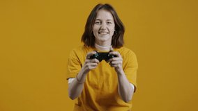 Portrait of emotional girl playing video game holding joystick then enjoying victory on yellow color background. People and entertainment concept.