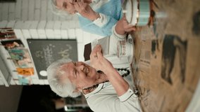 Happy senior friends sitting indoors in cafe drinking coffee or tea, eating chocolate, laughing and having nice time together. Vertical footage. - Powered by Shutterstock - Get 15% off with code: PIKWIZARD15