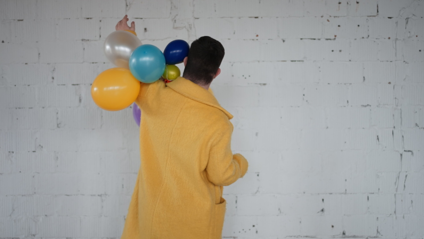 Happy boy with down syndrome posing with colourful baloons in front of white wall, during his birthday party.